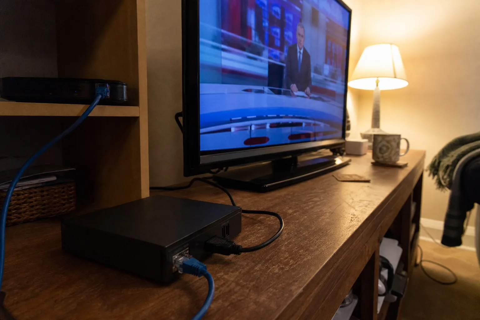 TV box wired with Ethernet to router and HDMI to TV; news program on screen.