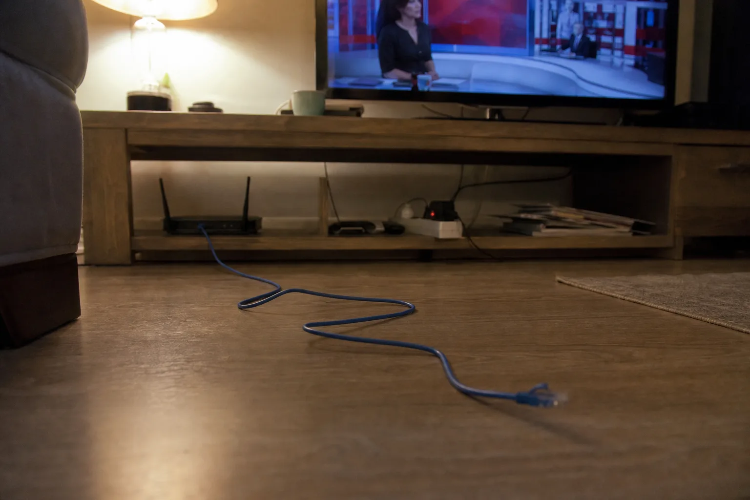 Unplugged blue Ethernet cable running from a router toward the TV cabinet.